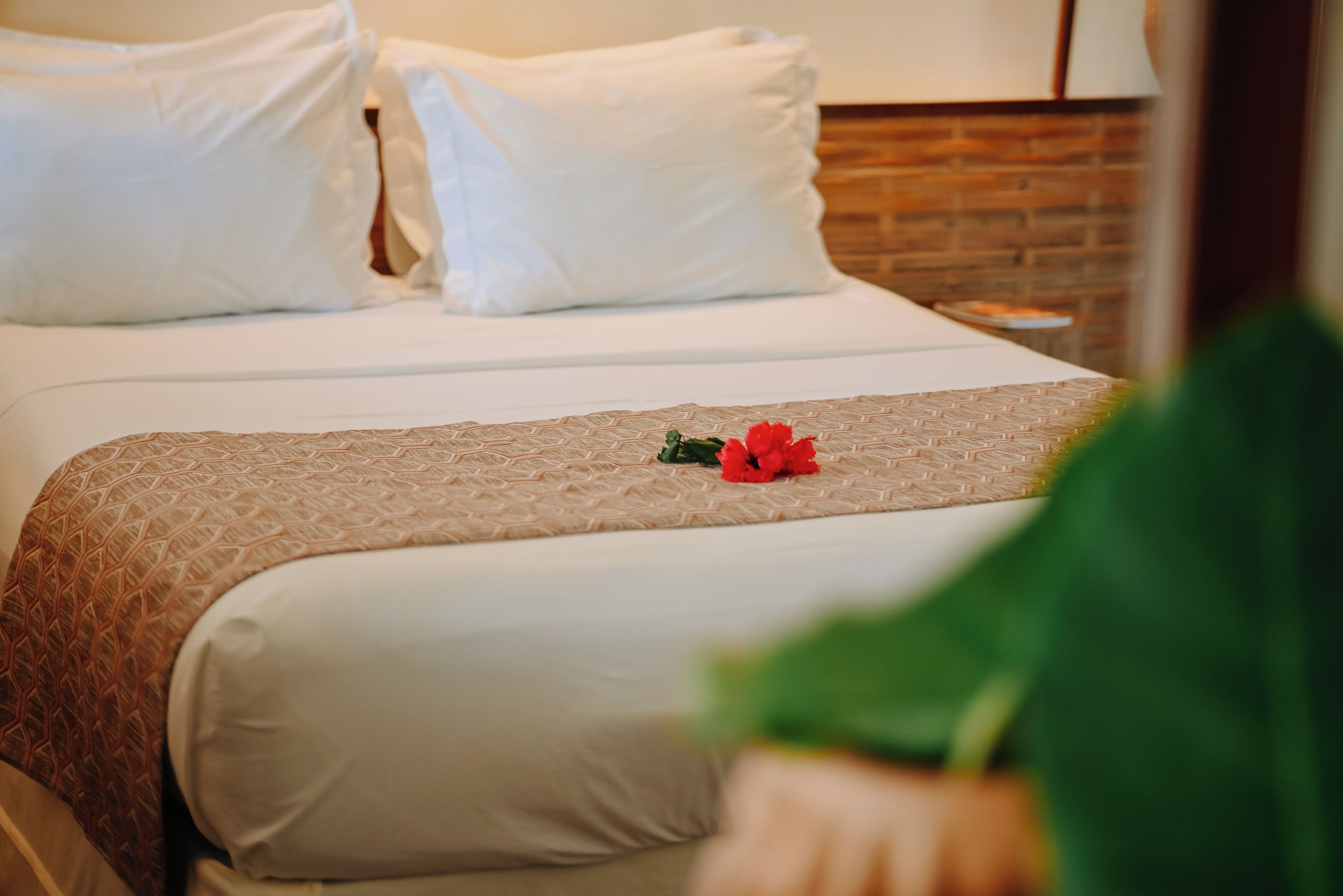 Quarto de hotel com uma cama bem arrumada, uma parede de tijolos e uma mesa de cabeceira com abajur.