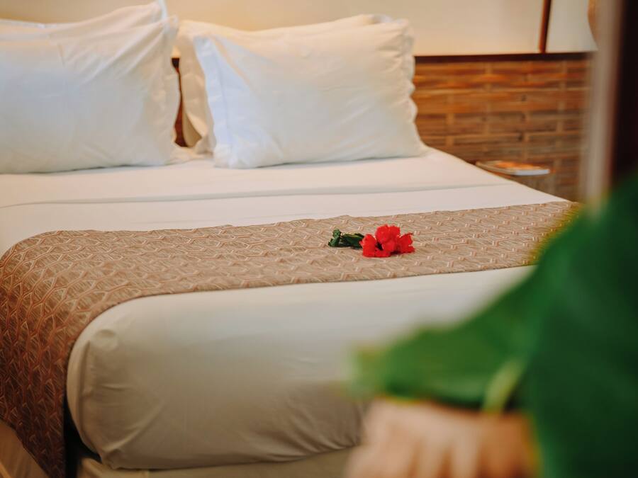 Habitación de hotel con una cama bien hecha, una pared de ladrillo y una mesita de noche con lámpara.