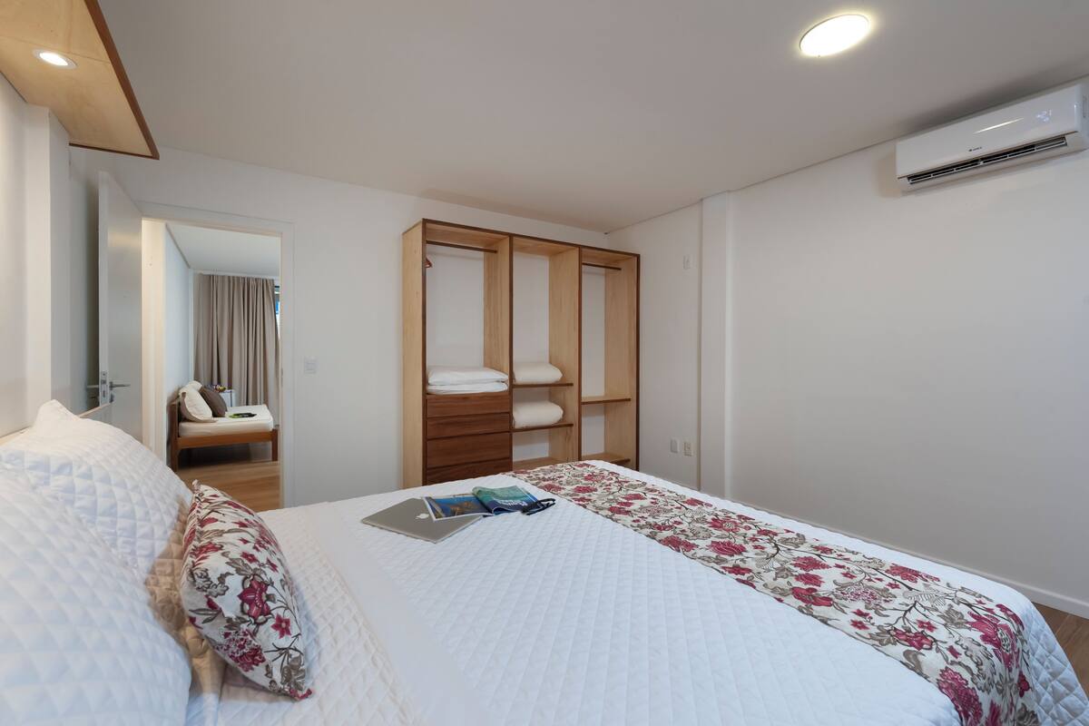 Un dormitorio ordenado con cama, un armario de madera y un equipo de aire acondicionado.