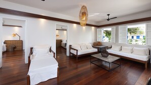 Amplia sala de estar con piso de madera, un sofá, una cama y una mesita de centro. Hay ventiladores de techo y una lámpara colgante.