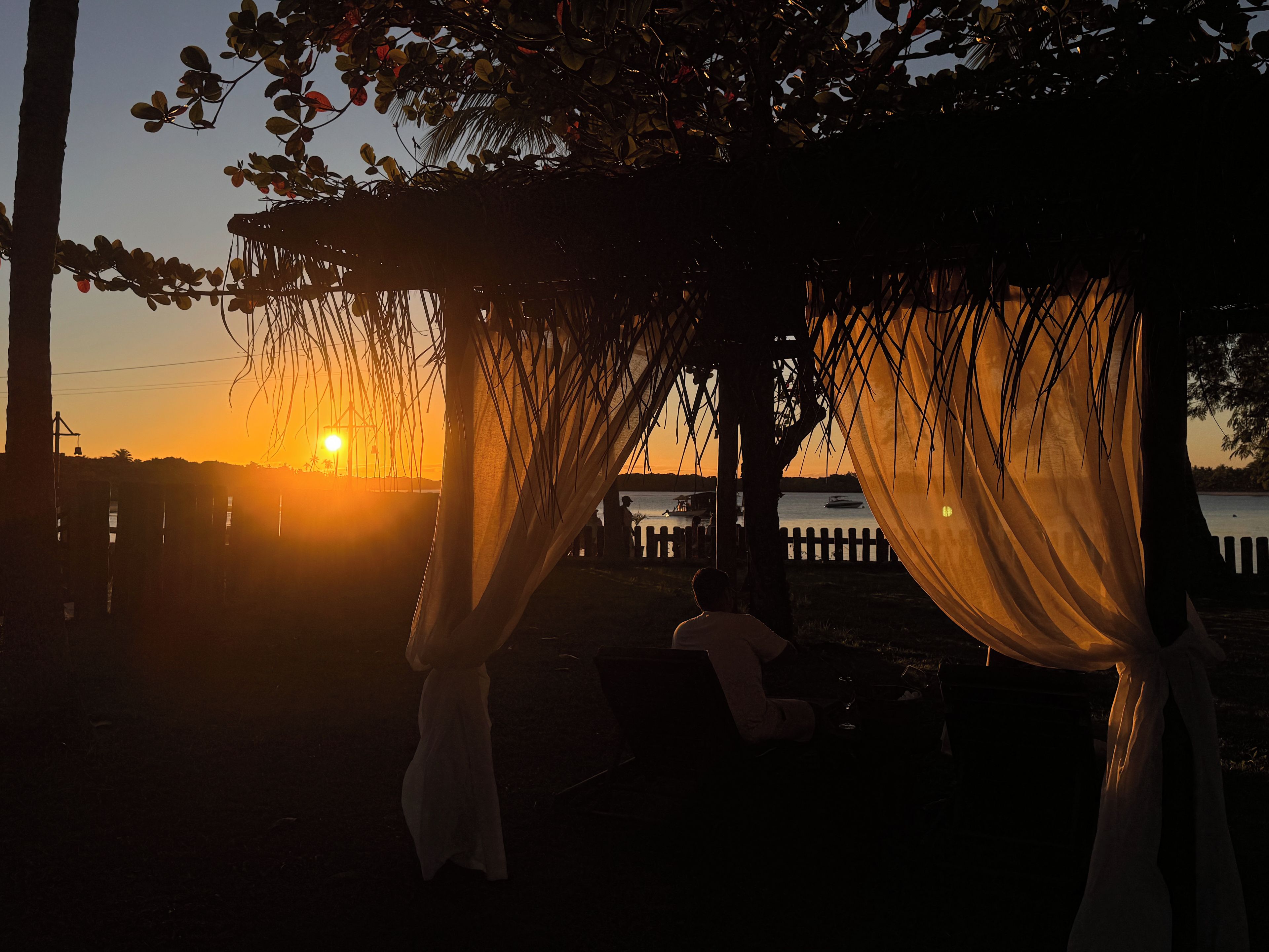 A sunset view from a covered outdoor area with a view of the water.
