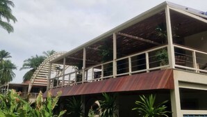Un edificio moderno con una galería techada, rodeado de abundante vegetación y palmeras.
