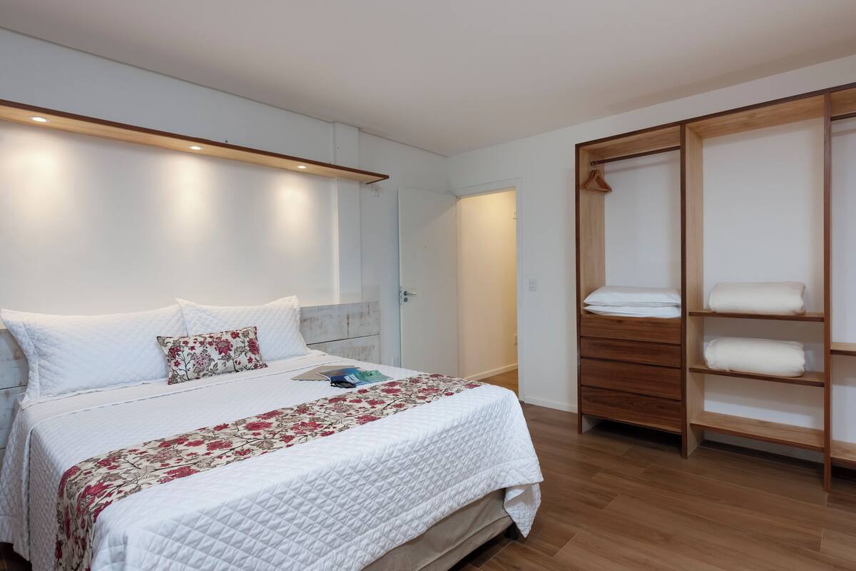 Un dormitorio con una cama, un armario de madera y una pared blanca.