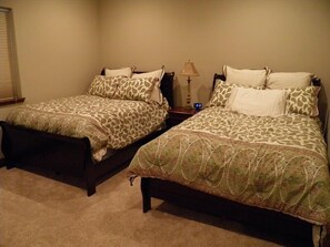 Two twin beds with patterned bedding, a bedside table with a lamp, and a window with blinds. - 3354 Red Lake Rd (South Lake Tahoe)