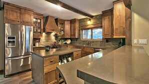 A modern kitchen with wooden cabinets, a stainless steel refrigerator, and a large island with a sink.