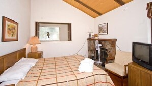 A bedroom with a bed, a window, a fireplace, a television, and a chair.