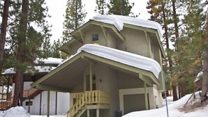 A two-story wooden house with a covered porch and a staircase leading to the entrance.