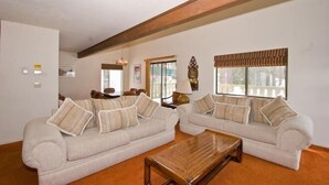 A living room with two beige sofas, a wooden coffee table, and a large window with blinds.