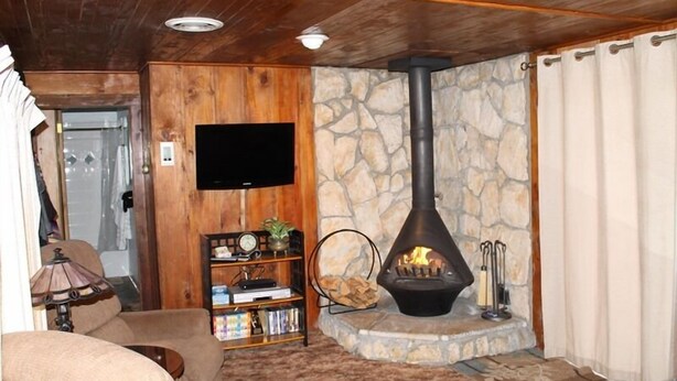 A cozy living room with a stone fireplace, wooden walls, a flat-screen TV, and a bookshelf. - 780 Merced Ave. (South Lake Tahoe)