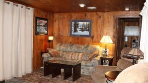 A cozy living room with wooden walls, a patterned sofa, a coffee table, and two lamps. - 780 Merced Ave. (South Lake Tahoe)