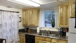 A compact kitchen with wooden cabinets, a built-in dishwasher, a sink, and a window with a view of the outside. - 780 Merced Ave. (South Lake Tahoe)