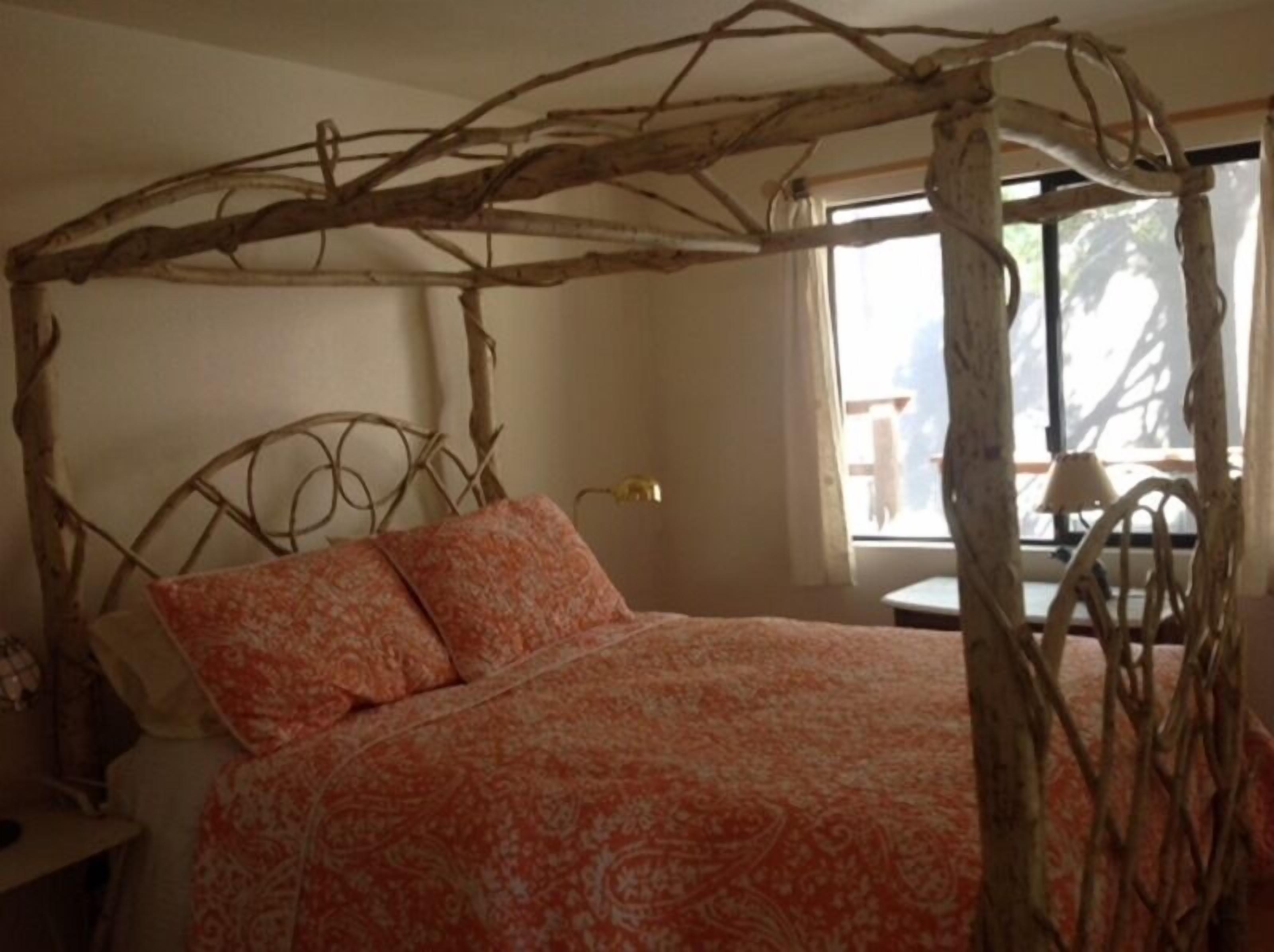 Un lit doté d’un baldaquin fait de branches, d’une couvre-lit à motifs et offrant une vue sur l’extérieur par une fenêtre.