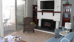 A living room with a fireplace, a television, and a dining area with a table and chairs. - 357 Ala Wai Unit 205 (South Lake Tahoe)