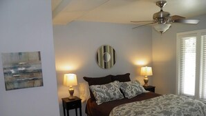 A bedroom with a bed, two bedside tables with lamps, a ceiling fan, a window with blinds, and a wall-mounted mirror. - 357 Ala Wai Unit 205 (South Lake Tahoe)