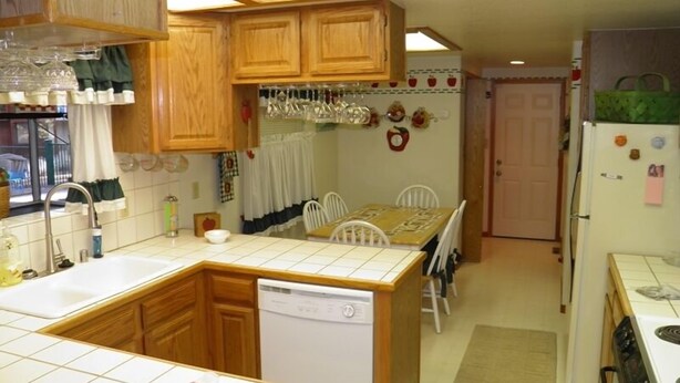 A compact kitchen with wooden cabinets, a dishwasher, a dining table with chairs, and a refrigerator.