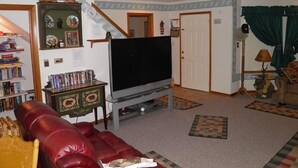 A living room with a flat-screen TV, a red leather couch, a bookshelf, and a staircase.