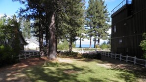 A fenced yard with a large tree, a building with a dark facade, and a view of the sea. - 777 Merced Ave (South Lake Tahoe)