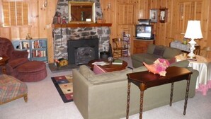A cozy log cabin interior with a stone fireplace, wooden furniture, and a television. - 777 Merced Ave (South Lake Tahoe)