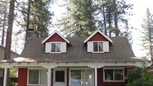 A two-story house with a red exterior and white trim, featuring a front porch with two white chairs and a bench. - 777 Merced Ave (South Lake Tahoe)