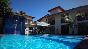 Une piscine à l’eau d’un bleu cristallin, entourée d’une terrasse en bois et bordée d’un bâtiment doté de balcons.