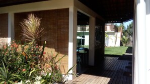 Un espace extérieur aménagé en terrasse, avec un sol en bois, un coin salon couvert et une vue sur un jardin arrière.