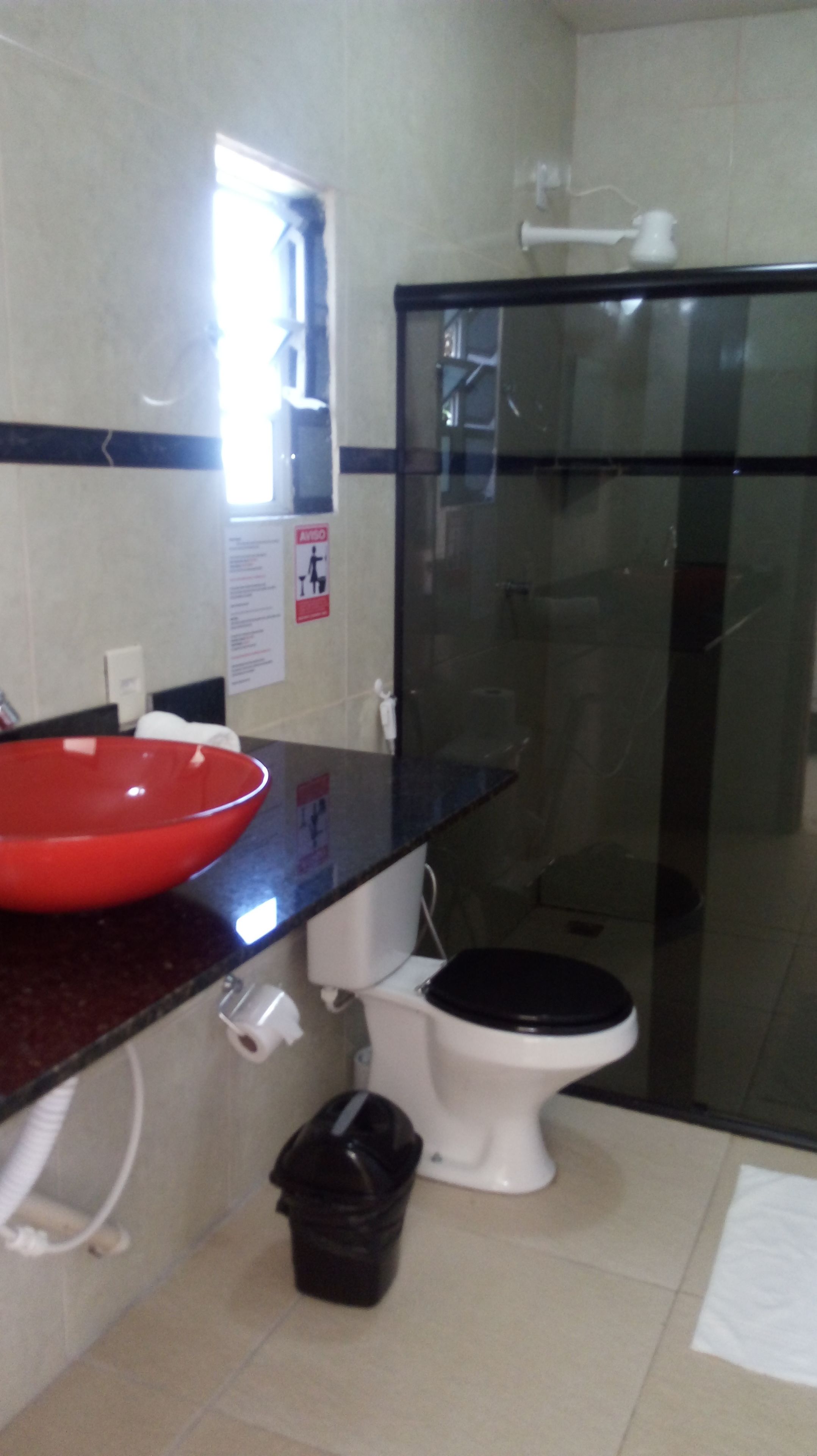 A bathroom with a red basin, a white toilet, and a glass shower enclosure.