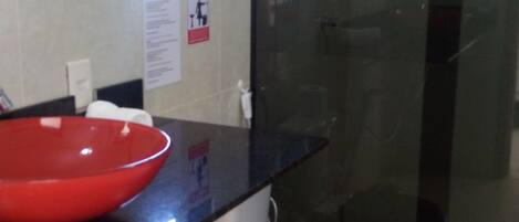 A bathroom with a red basin, a white toilet, and a glass shower enclosure.