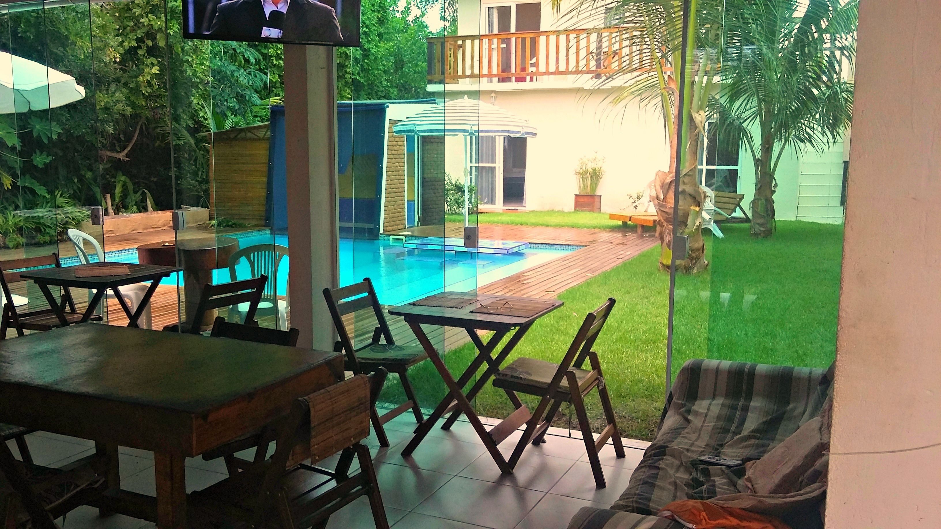 An outdoor patio area with a pool, wooden furniture, and a view of a house in the background.