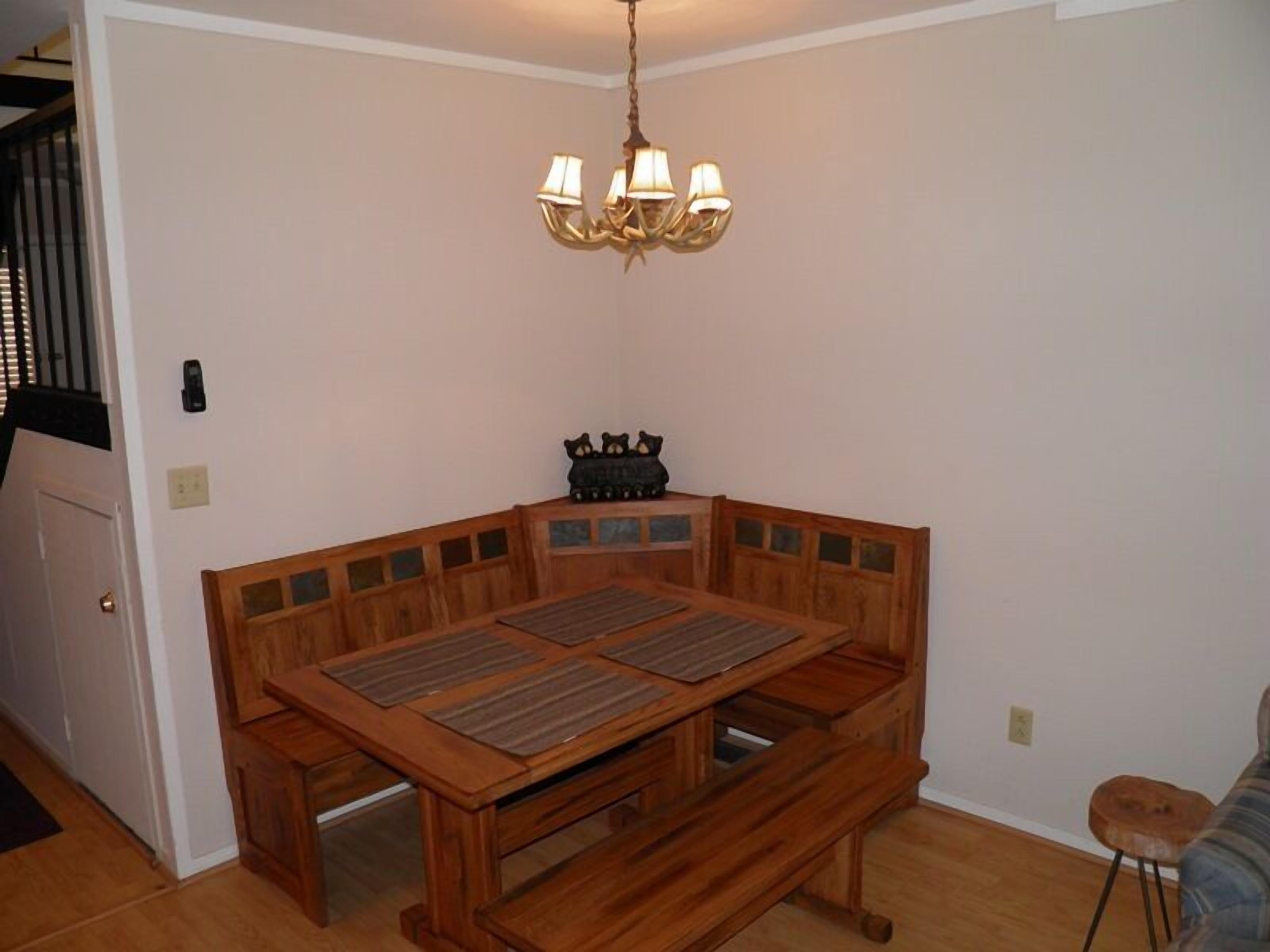 A dining area with a wooden table and bench, a chandelier, and a bear figurine on the wall.