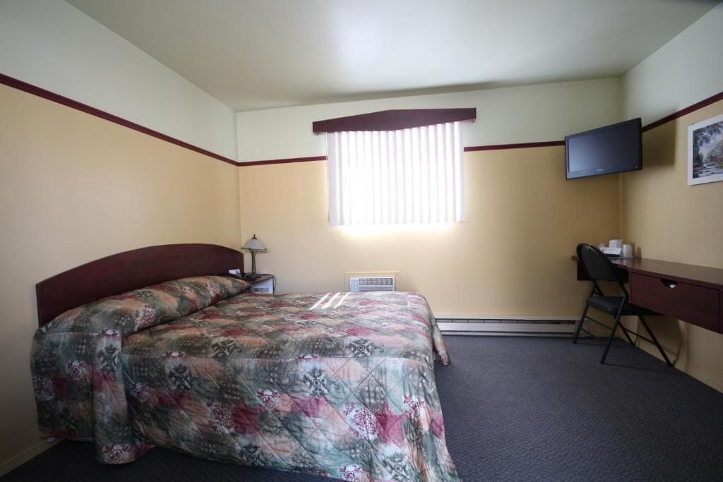 A hotel room with a bed, a desk, a chair, a television, and a window with blinds.