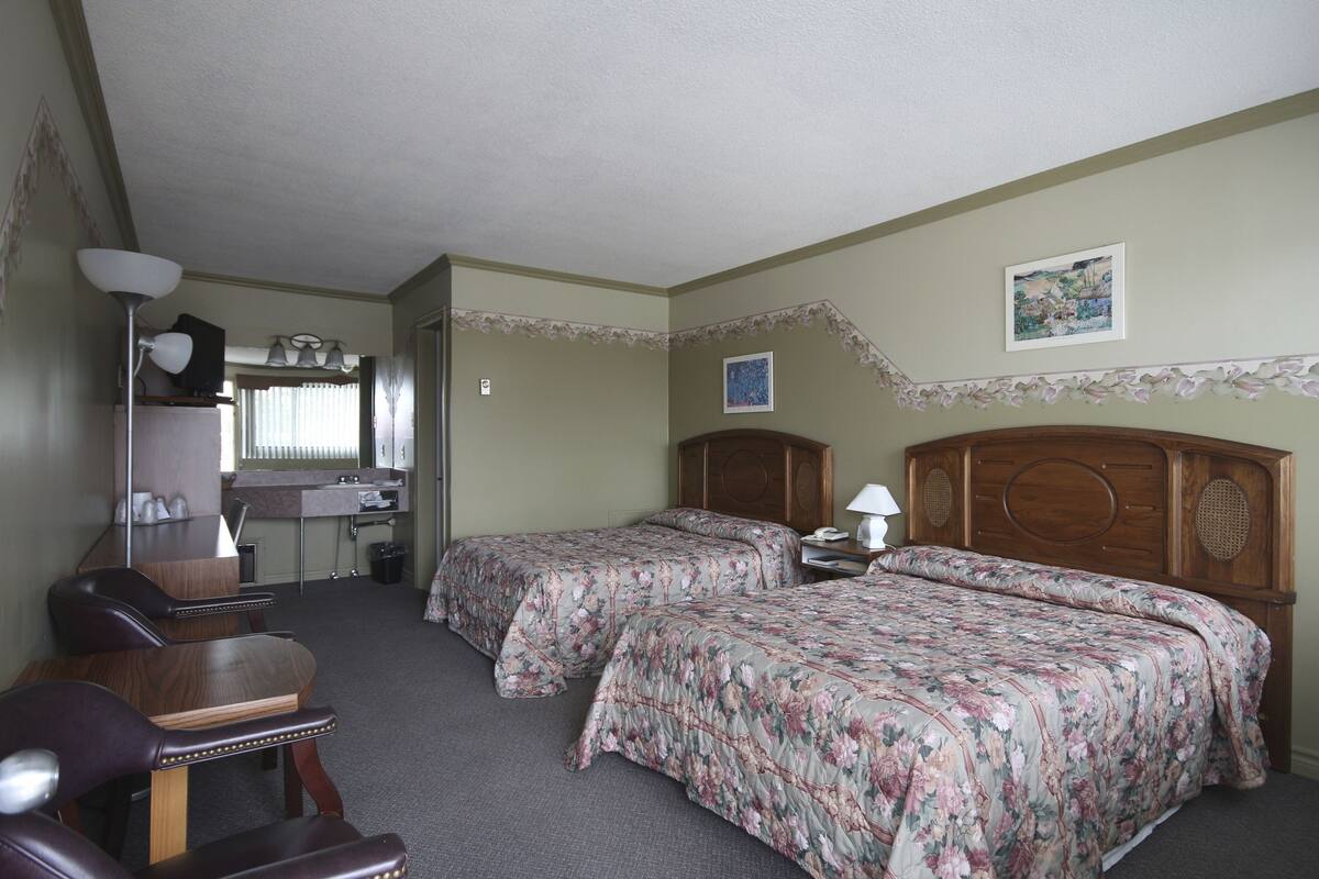 Ein Hotelzimmer mit zwei Betten, einem Schreibtisch, einem Stuhl, einem Spiegel und einem durchgegangenen Tür erkennbaren Badezimmer.