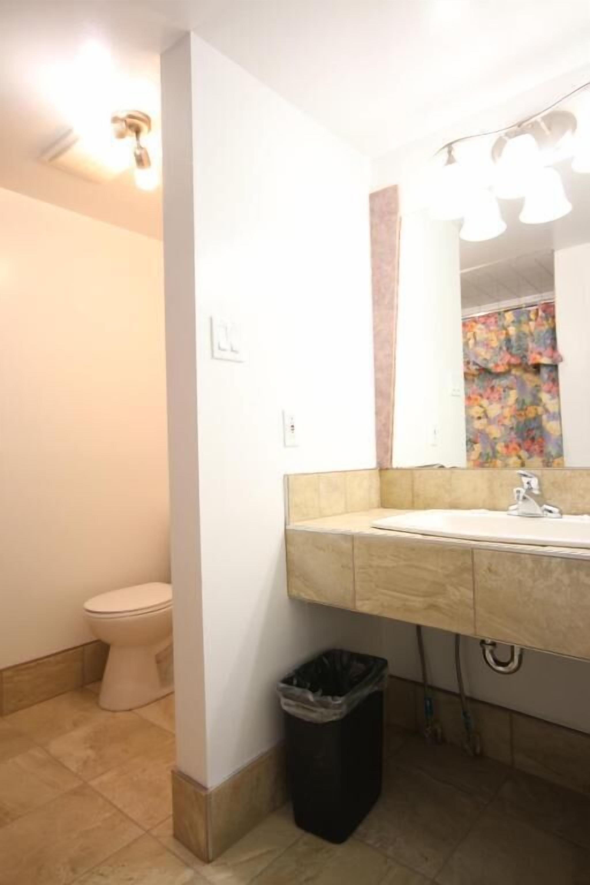 A bathroom with a toilet, sink, mirror, and a trash bin.