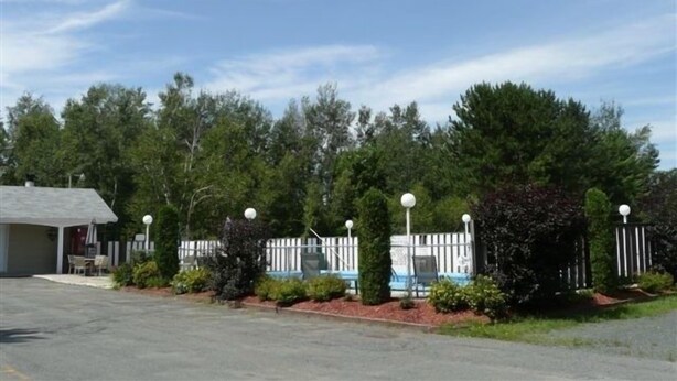 A parking lot with a building, a white fence, and trees. - Motel Marie-Dan (Sainte-Eulalie)