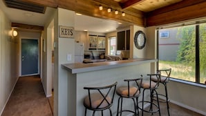 A kitchen with a bar area, bar stools, a clock, and a view of the outdoors.