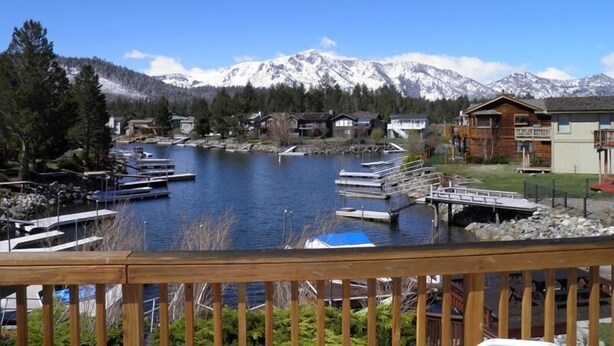 A lakeside property with docked boats, a wooden deck, and a mountain backdrop. - 584 Alpine Dr (South Lake Tahoe)