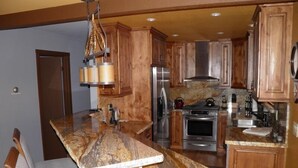 A kitchen with wooden cabinets, granite countertops, stainless steel appliances, and a bar area with seating. - 584 Alpine Dr (South Lake Tahoe)