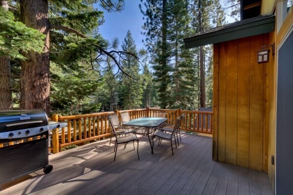 A wooden deck with a table and chairs, surrounded by tall trees.