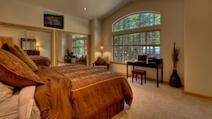 Ein Schlafzimmer mit einem großen Bett, einem Schreibtisch und einem Fenster mit Blick auf Bäume.