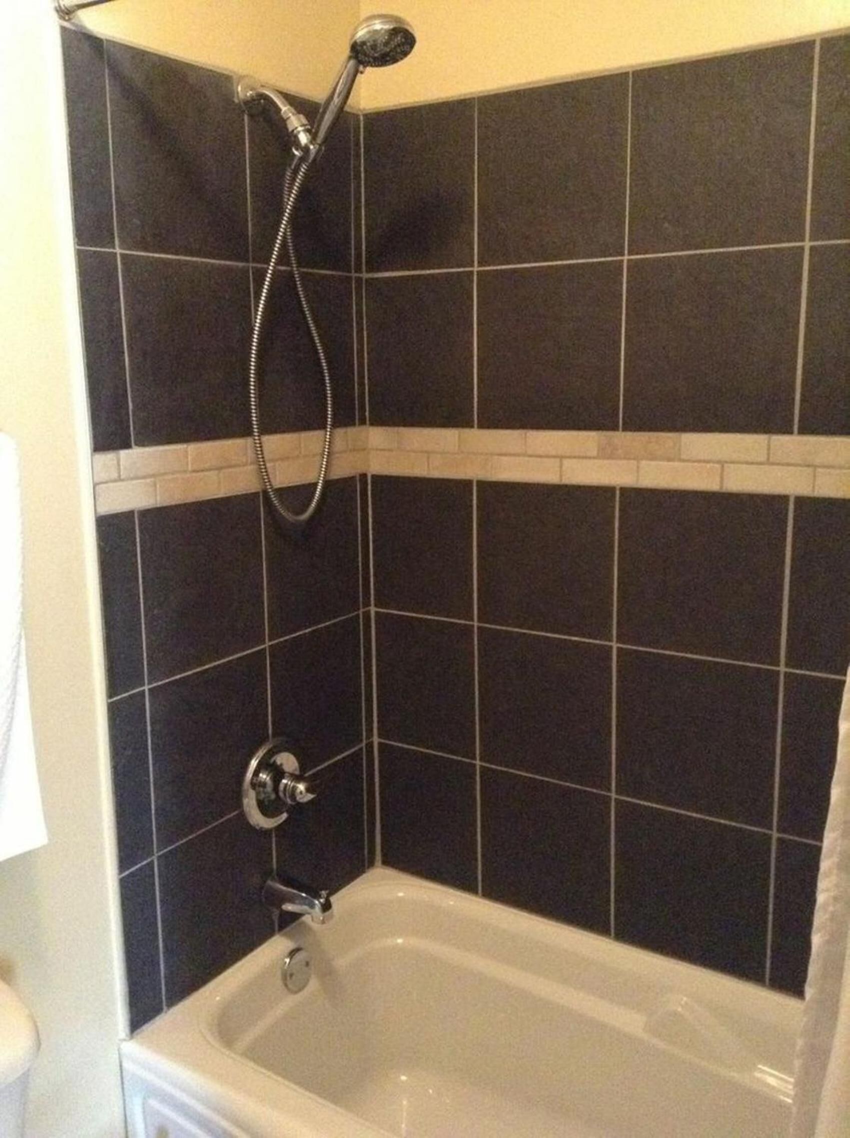 A bathroom with a bathtub, a shower, and dark tiled walls.