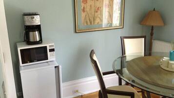 A dining area with a round glass table, white chairs, a coffee maker, a microwave, and a framed floral painting on the wall.