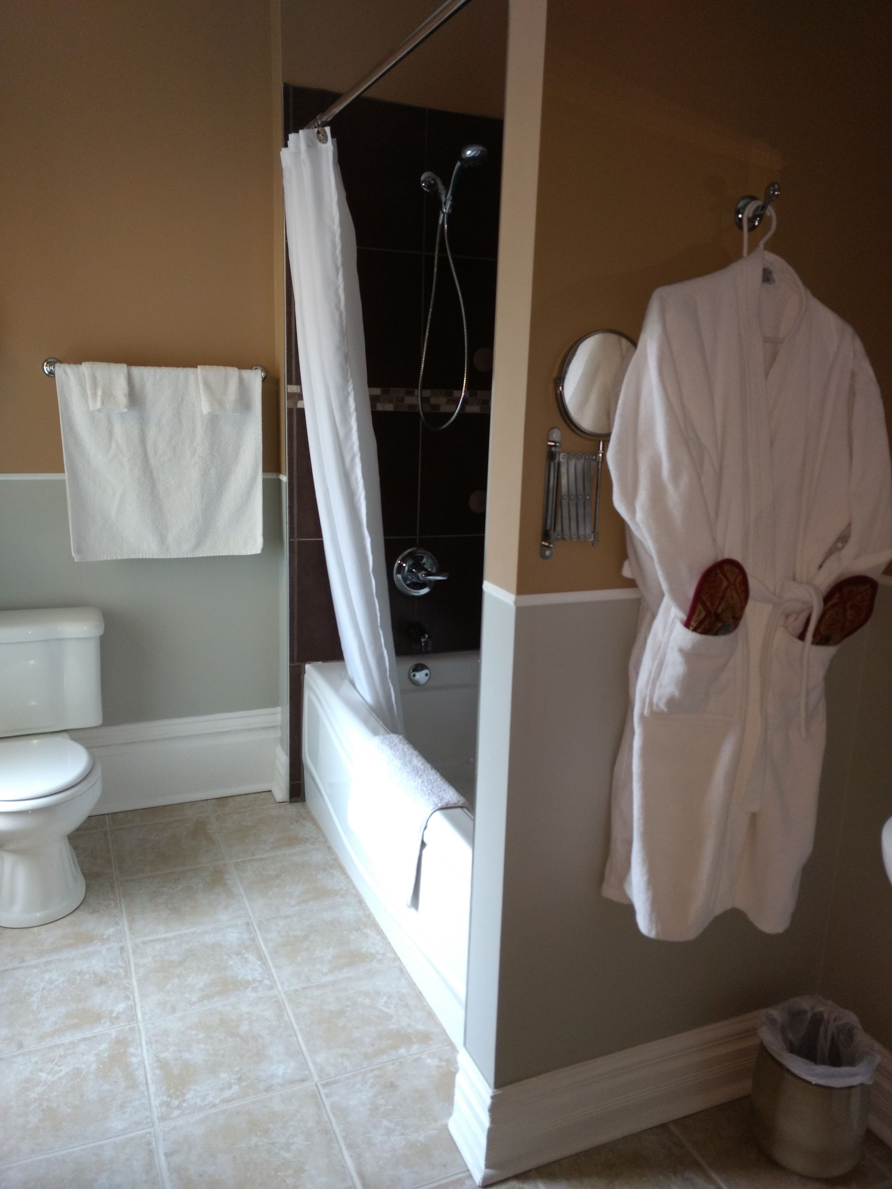 A bathroom with a toilet, a shower, and a bathtub. There is a towel hanging on the wall and a robe hanging on a hook.