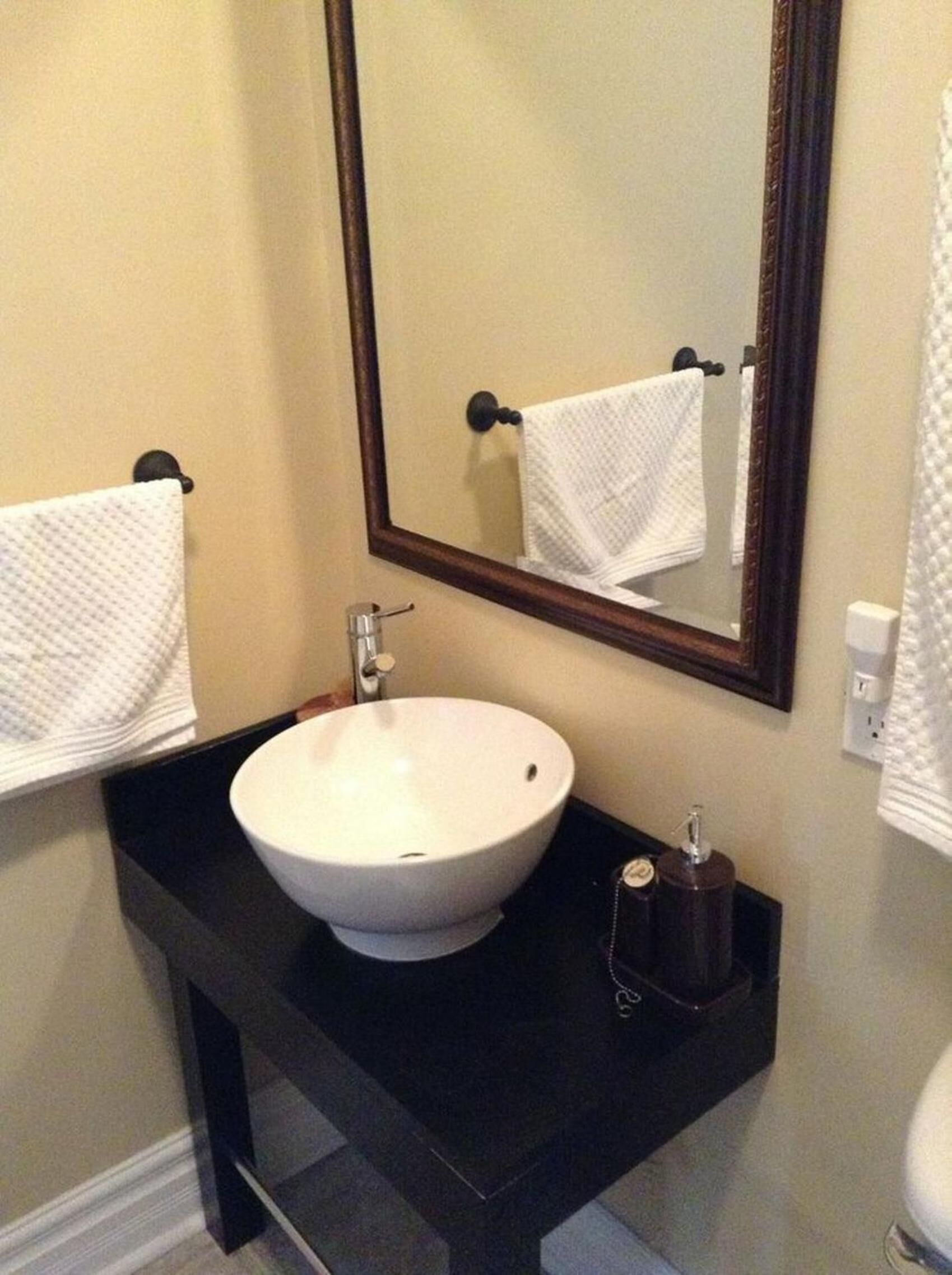 Un bagno con lavandino bianco, piano di lavoro nero e specchio con cornice in legno.