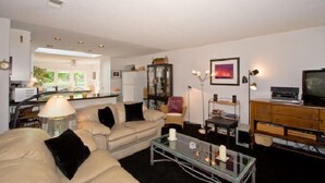 A living room with a sofa, coffee table, and a television. There is a cabinet and a lamp.