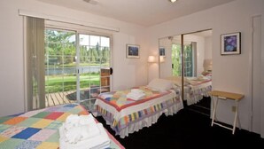A hotel room with a large bed, a smaller bed, a desk, and a balcony with a view of greenery.