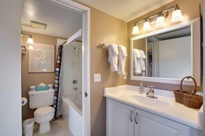 A bathroom with a toilet, shower, sink, and a mirror with lights.
