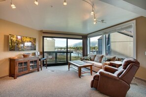 A spacious living room with a large window, a sofa, a recliner, a coffee table, and a cabinet.