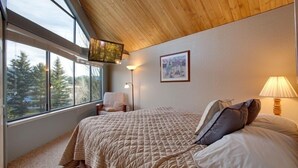 Una camera da letto con una grande finestra, un letto con copria letto trapuntato, una sedia e una lampada.