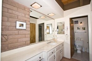 Un baño moderno con un espejo grande, tocador blanco y un inodoro a la vista.