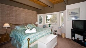 A bedroom with a bed, bedside table, lamp, TV, and windows.