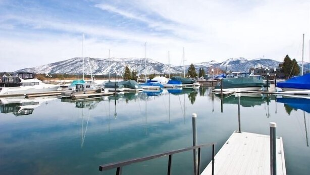 A marina with boats docked, a wooden dock, and snow-capped mountains in the background.